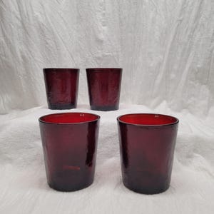 May include: Four dark red glass tumblers with a textured surface. The tumblers are arranged in a square shape.