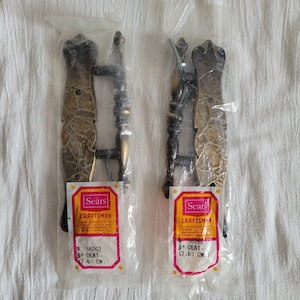 May include: Two antique brass cabinet door pulls with a decorative design. The pulls are packaged in plastic bags with Sears Craftsman labels. The labels indicate the pulls are 3 inches (7.6 cm) in size.