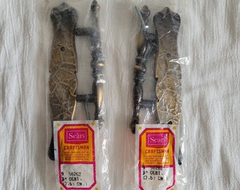 May include: Two antique brass cabinet door pulls with a decorative design. The pulls are packaged in plastic bags with Sears Craftsman labels. The labels indicate the pulls are 3 inches (7.6 cm) in size.