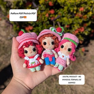 May include: Three crocheted dolls in the image, each with a strawberry theme. The dolls have pink hats, red hair, and are wearing dresses. The text in the image says "Pattern PDF/Patr&oacute;n PDF ESP" and "DIGITAL PRODUCT - NO PHYSICAL ITEM WILL BE SHIPPED."