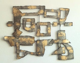 May include: Abstract metal wall art in gold and grey tones, featuring geometric shapes. The artwork includes squares, rectangles, and irregular forms, connected by thin metal rods, creating a modern, textured design for a wall.