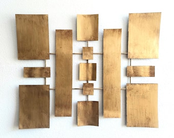 May include: Gold metal wall art with a geometric design. The art is made up of multiple rectangular pieces of metal that are arranged in a grid pattern.