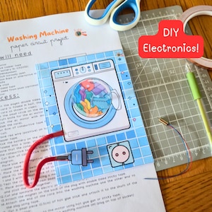 Op de afbeelding: Een doe-het-zelf elektronica project met een papieren circuit van een wasmachine. De illustratie toont een wasmachine met een stekker en stopcontact, verbonden door rode draden. De tekst "DIY Electronics!" staat in een rode rechthoek.