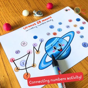 May include: An educational activity sheet with a cartoon Uranus illustration and the text "Uranus 28 moons connecting numbers activity". The sheet has numbered circles to connect, with a black marker pointing at the image. The words "Connecting numbers activity!" are in a red banner.