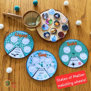 May include: Three colourful, circular learning aids for teaching the states of matter. Each wheel has a different state of matter: liquid, gas, and solid. Each wheel has a tick or a cross to indicate whether the state of matter can be weighed, compressed, or occupies space. The wheels are on a wooden surface with a magnifying glass and small white balls.