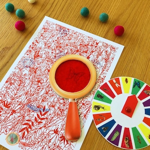 May include: A red magnifying glass with a butterfly design on the lens. The magnifying glass is on a white background with a red and white pattern. There is a colorful wheel with different insects on it.