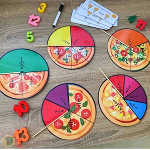 Puede incluir: Un conjunto de cinco círculos de fracciones de pizza coloridos, cada uno dividido en diferentes fracciones. Los círculos son de cartón y tienen un diseño de pizza. Las fracciones están escritas en los círculos en texto negro. Los círculos están dispuestos en círculo sobre una superficie de madera. También hay algunos bloques de números coloridos en la superficie.