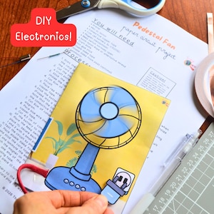 Peut inclure: Projet d'électronique DIY avec un ventilateur à circuit en papier. Le ventilateur, bleu et jaune, est relié à une prise par un cordon rouge. L'image comprend des instructions, une règle, des ciseaux et du ruban de cuivre.