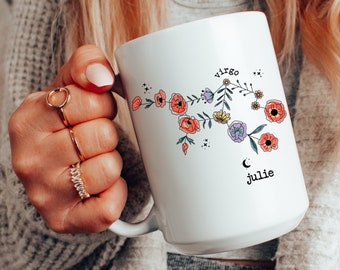 May include: White ceramic mug with a floral design depicting the Virgo zodiac sign. The mug also includes the name "Julie" and a crescent moon.