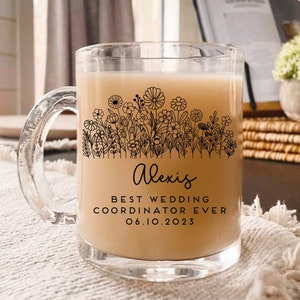 Może przedstawiać: Przezroczysty kubek ze szkła z czarnym wzorem kwiatowym i tekstem "Alexis Best Wedding Coordinator Ever 06.10.2023". Kubek jest wypełniony jasnobrązowym płynem.
