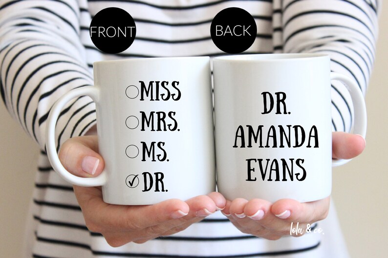 May include: Two white coffee mugs. The mug on the left has a checklist with the options "Miss", "Mrs.", "Ms.", and "Dr." with the last option checked. The mug on the right says "Dr. Amanda Evans".