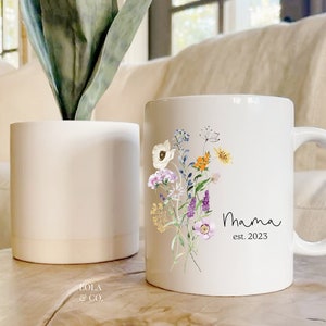 May include: White ceramic mug with a floral design and the text "Mama est. 2023".