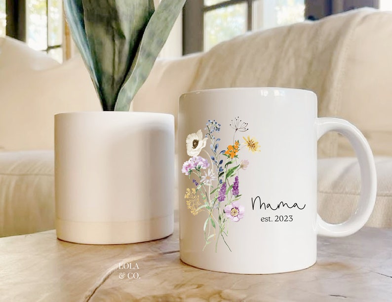 May include: White ceramic mug with a floral design and the text "Mama est. 2023".