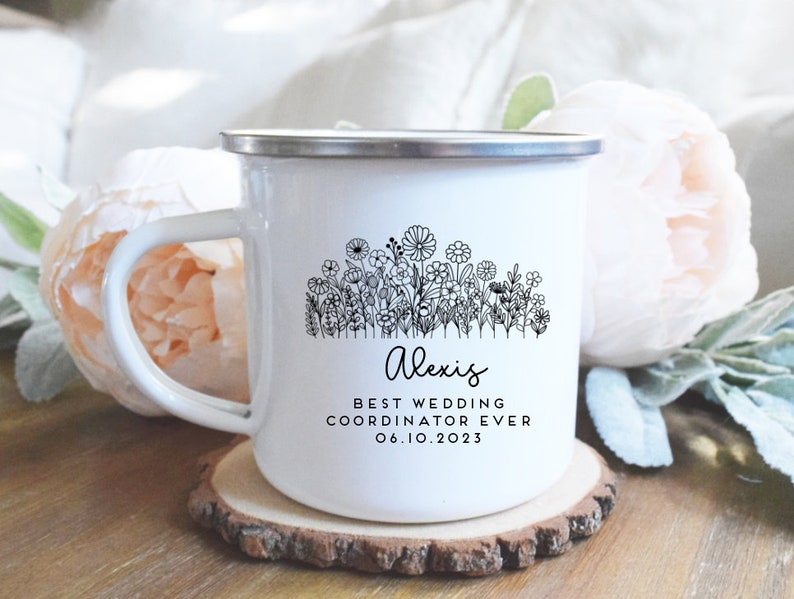 Może przedstawiać: Biały kubek emaliowany z czarnym wzorem kwiatowym i tekstem "Alexis Best Wedding Coordinator Ever 06.10.2023".