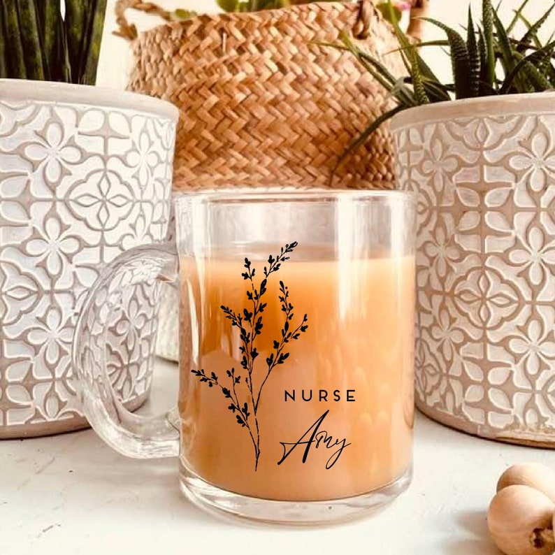 Pu&ograve; includere: Una tazza di vetro trasparente con un motivo floreale nero e il testo "NURSE Amy". La tazza &egrave; piena di un liquido marrone chiaro.