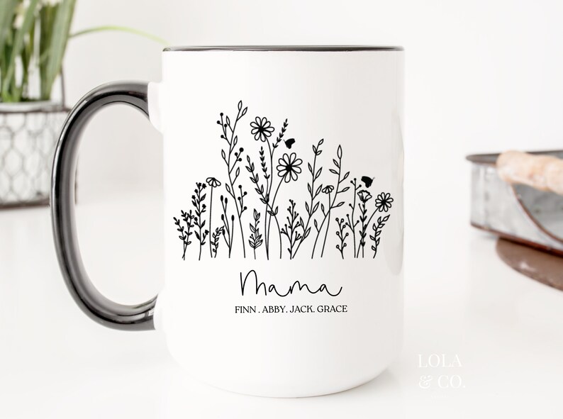 May include: White ceramic mug with a black rim and handle. The mug features a black and white illustration of flowers and the word "Mama" with the names Finn, Abby, Jack, Grace underneath.