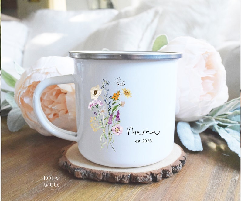 May include: White enamel mug with a floral design and the text "Mama est. 2023".