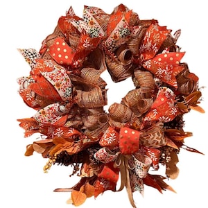 May include: A fall-themed wreath with orange, brown, and white ribbon and mesh. The wreath is decorated with fall leaves and pinecones.