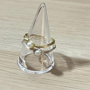 May include: Two gold and silver wire rings with white pearl accents on a clear plastic ring holder.