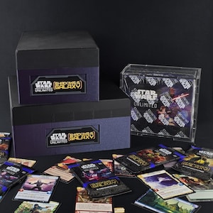 May include: A collection of Star Wars: Unlimited trading card game products. The image shows two black boxes with the game's logo, a clear display case, and several booster packs and individual cards scattered on a dark surface. The game's name and logo are visible.