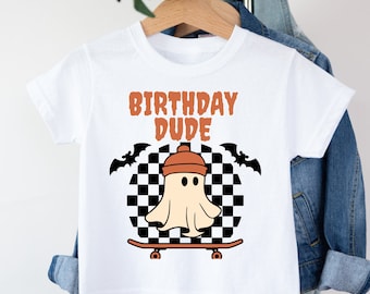 May include: White t-shirt with a graphic of a ghost wearing a beanie and skateboarding on a checkered background. The text "Birthday Dude" is above the ghost.