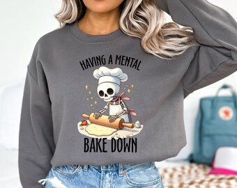 May include: Gray sweatshirt with a skeleton wearing a chef hat and apron rolling out dough. The text on the sweatshirt reads "Having a mental bake down."