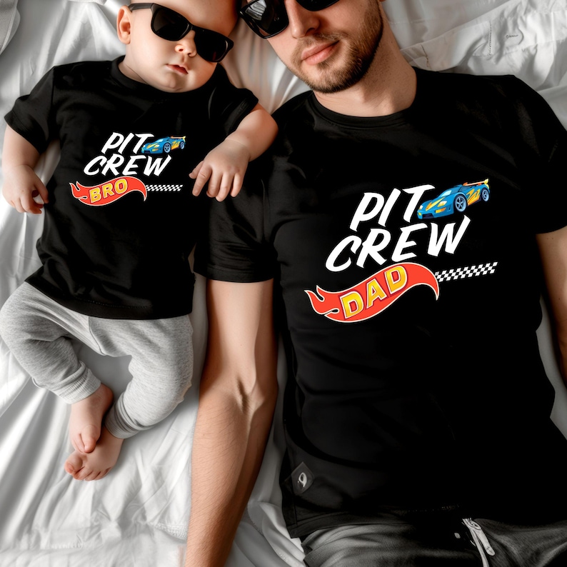 May include: Matching black t-shirts for a father and son. The father's shirt says "Pit Crew Dad" with a cartoon race car and flames. The son's shirt says "Pit Crew Bro".