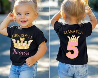 Pode incluir: Camiseta preta com um design de coroa dourada e rosa e o texto "Her Royal Fiveness" na frente. A parte de trás da camiseta tem o nome "Makayla" acima de uma coroa e o número "5". A criança está usando shorts jeans.