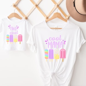 May include: Two white t-shirts with a matching ice cream theme. The larger shirt says "cool mama" with four colorful ice cream pops. The smaller shirt says "two cool" with three ice cream pops.