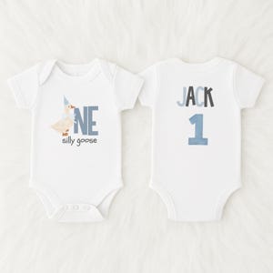 May include: Two white baby onesies. One has a goose graphic with the text "NE silly goose". The other has the name "JACK" and the number "1". The text and graphics are in shades of blue and gray.