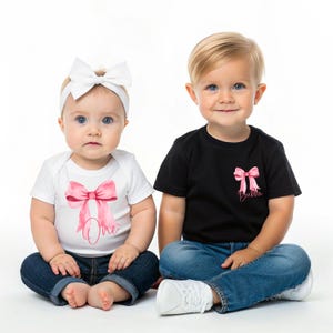 May include: Two children wearing matching shirts with pink bows and the word "One" and "Bubba" on them. The girl is wearing a white headband with a bow. The boy is wearing blue jeans and white sneakers.