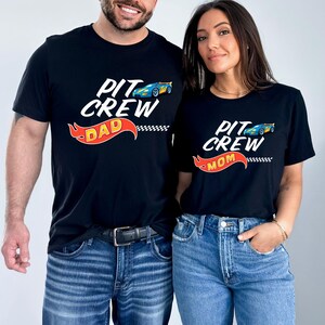 May include: A couple wearing matching black t-shirts with a racing car graphic and the text "Pit Crew Dad" and "Pit Crew Mom".