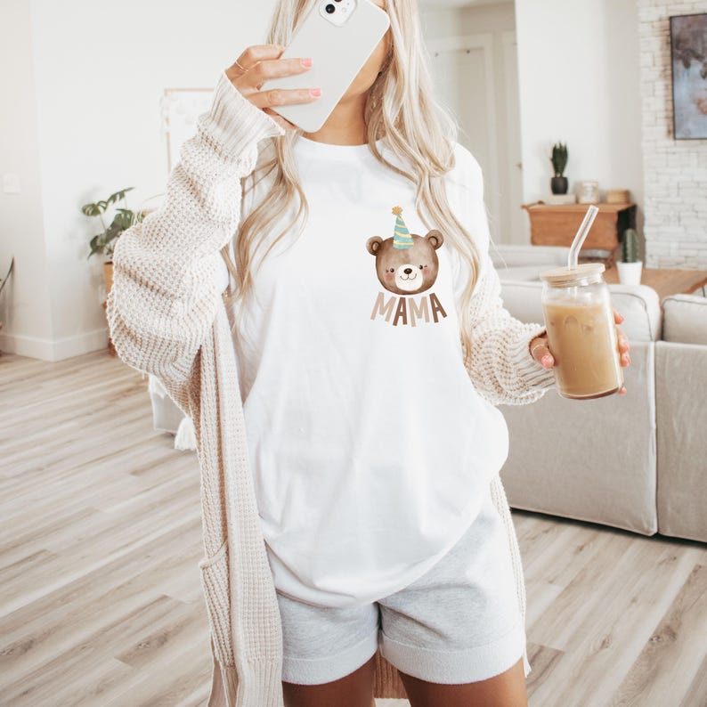 May include: White t-shirt with a brown bear wearing a party hat and the word "MAMA" printed on the front.