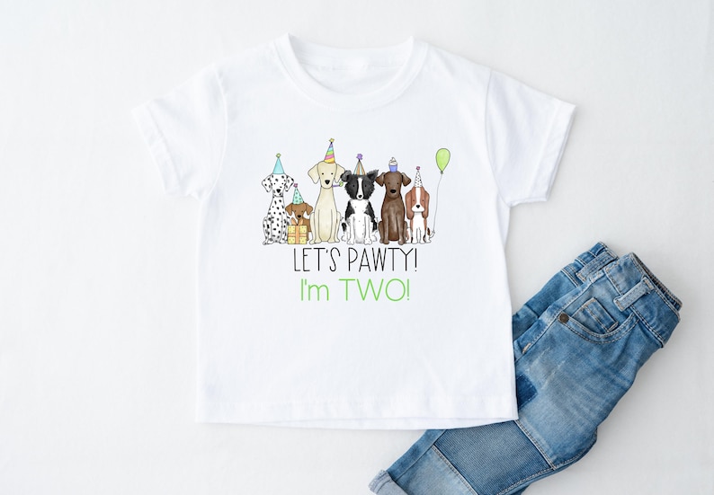 Op de afbeelding: Wit T-shirt met een afbeelding van vijf honden die feestmutsen dragen en een cadeau vasthouden. De tekst "Let's Pawty! I'm Two!" staat onder de afbeelding.