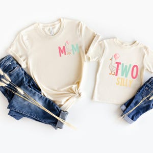 May include: Two beige t-shirts with a goose graphic. The larger shirt says "MOM" in pink, teal, and yellow letters. The smaller shirt says "TWO SILLY" in pink, teal, and yellow letters.