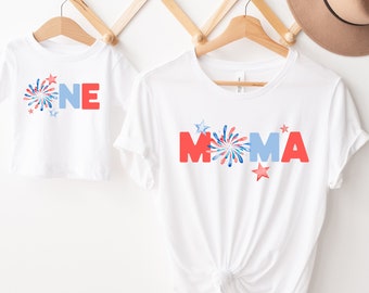 May include: Two white t-shirts with red, white, and blue firework designs. One shirt says "MAMA" and the other says "ONE".