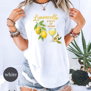 May include: White t-shirt with a watercolor design featuring lemons, a glass of limoncello, and the text "Limoncello State of Mind" in gold lettering. The shirt has a crew neck and short sleeves.