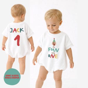 May include: White short-sleeve bubble romper with the text "It's FUN to be ONE" and a baby wearing a party hat. The back of the romper has the name "JACK" and the number "1". The romper is designed for a baby's first birthday.