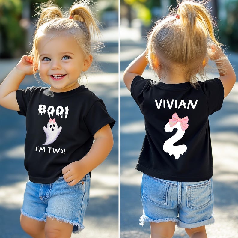 May include: Black t-shirt with a ghost graphic and the text "BOO! I'M TWO!" on the front. The back of the shirt has the name "VIVIAN" and the number "2" with a pink bow. The child is wearing blue denim shorts.