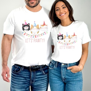 May include: Two white t-shirts with a graphic of three cats wearing party hats and a banner that says "Let's Pawty!"