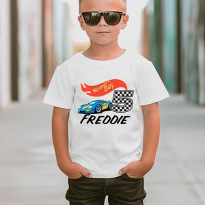May include: White t-shirt with a blue race car graphic, a red and yellow flame, and the text "Birthday Boy" and "FREDDIE".
