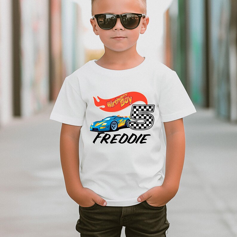 May include: White t-shirt with a blue race car graphic, a red and yellow flame, and the text "Birthday Boy" and "FREDDIE".