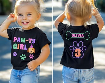 May include: A black t-shirt with a paw print design and the text "PAW-TY GIRL" in rainbow colors. The back of the shirt has a bone with the name "OLIVIA" and a paw print with the number "3" inside.
