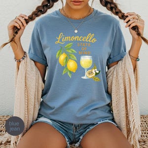 May include: Blue jean t-shirt with the words "Limoncello State of Mind" in yellow script. The shirt features a watercolor illustration of lemons, leaves, and a glass of limoncello.