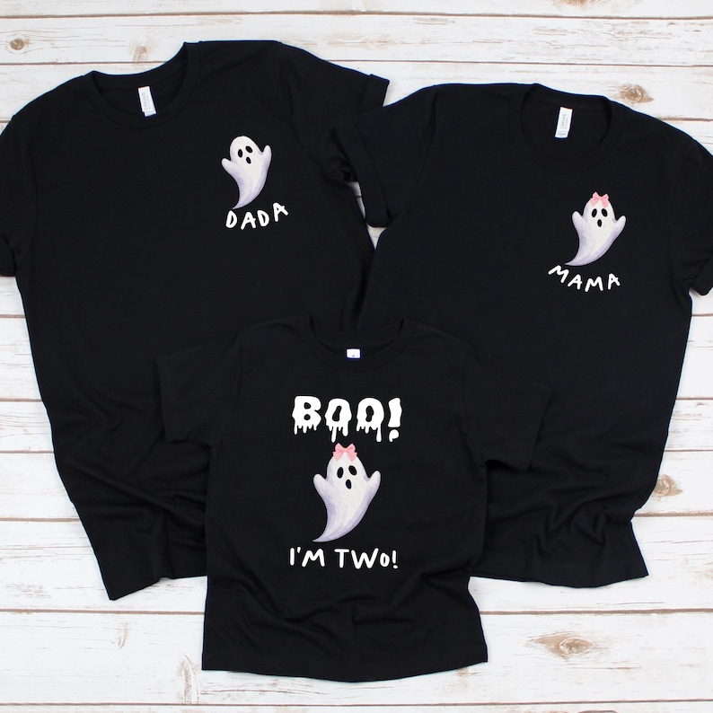 May include: Three black t-shirts with white ghost graphics. One shirt says "DADA", another says "MAMA", and the third says "BOO! I'M TWO!". The ghost graphics have pink bows. Perfect for a family Halloween.