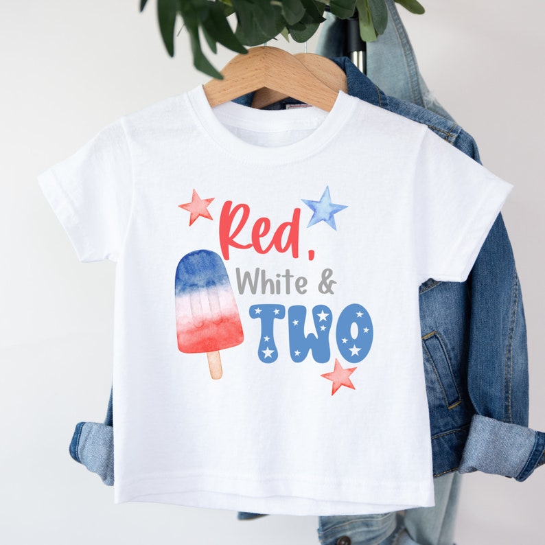 K&ouml;nnte beinhalten: Wei&szlig;es T-Shirt mit einem roten, wei&szlig;en und blauen Eis am Stiel-Motiv und dem Text "Red, White & Two" mit Sternen.