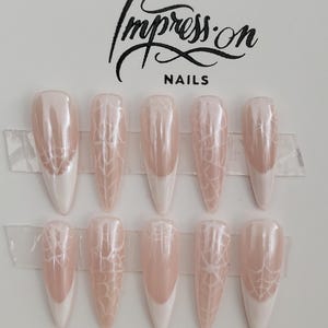 Op de afbeelding: Set van tien nudekleurige press-on nagels met een wit spinnenwebontwerp en een witte french tip.