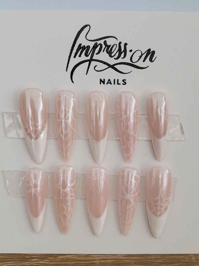 Op de afbeelding: Set van tien nudekleurige press-on nagels met een wit spinnenwebontwerp en een witte french tip.