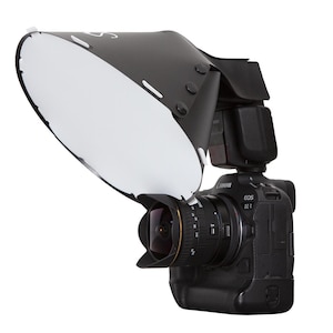 Könnte beinhalten: Eine schwarze Canon EOS R6 Kamera mit Objektiv und Blitzgerät. Ein schwarz-weißer Lichtmodifikator ist am Objektiv angebracht. Die Kamera befindet sich auf weißem Hintergrund. Fotoausrüstung.