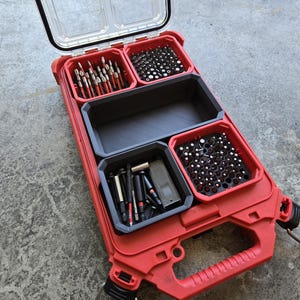 May include: Open red toolbox with a clear lid, filled with various black and silver drill bits and accessories. The toolbox has a black interior with multiple compartments for organization. The handle is red and the case is made of durable plastic.